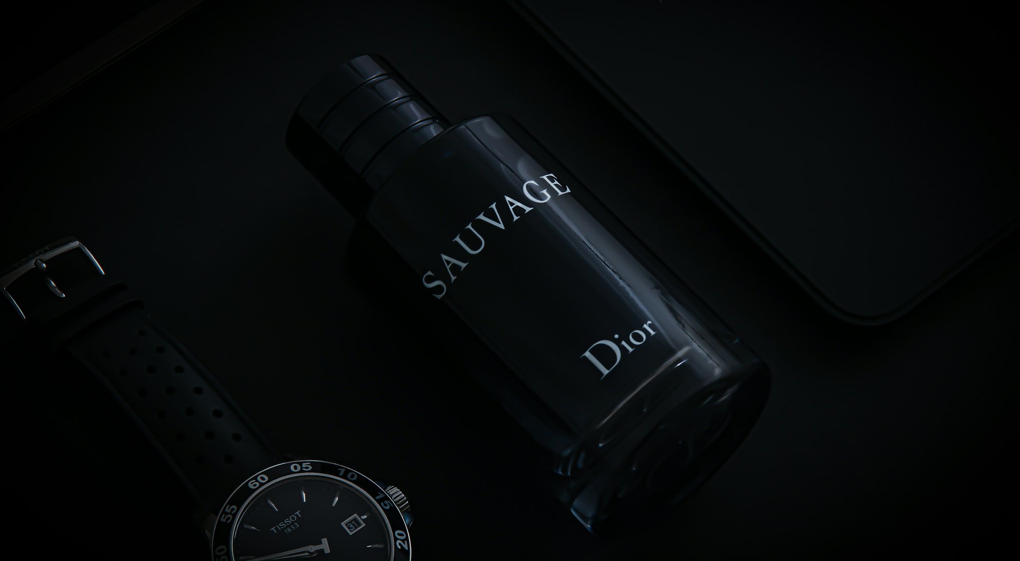 Frasco de perfume oscuro junto a un reloj, luz baja de estudio